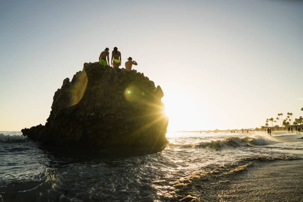 Silhouette of adult friends on rock formation at sunset, Newport Beach, California, USA