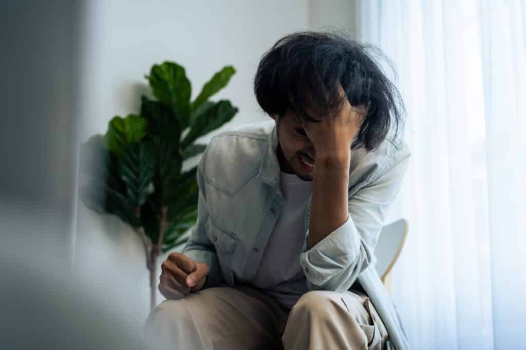 Asian young upset depressed man sitting alone in living room at home. Attractive unhappy male feeling very sad, lonely and frustrated with life problem think of money debt, budget loss, bankruptcy.