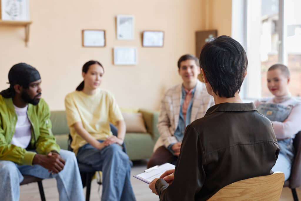 Rear view of psychologist sitting on chair and talking to people during psychotherapy in office