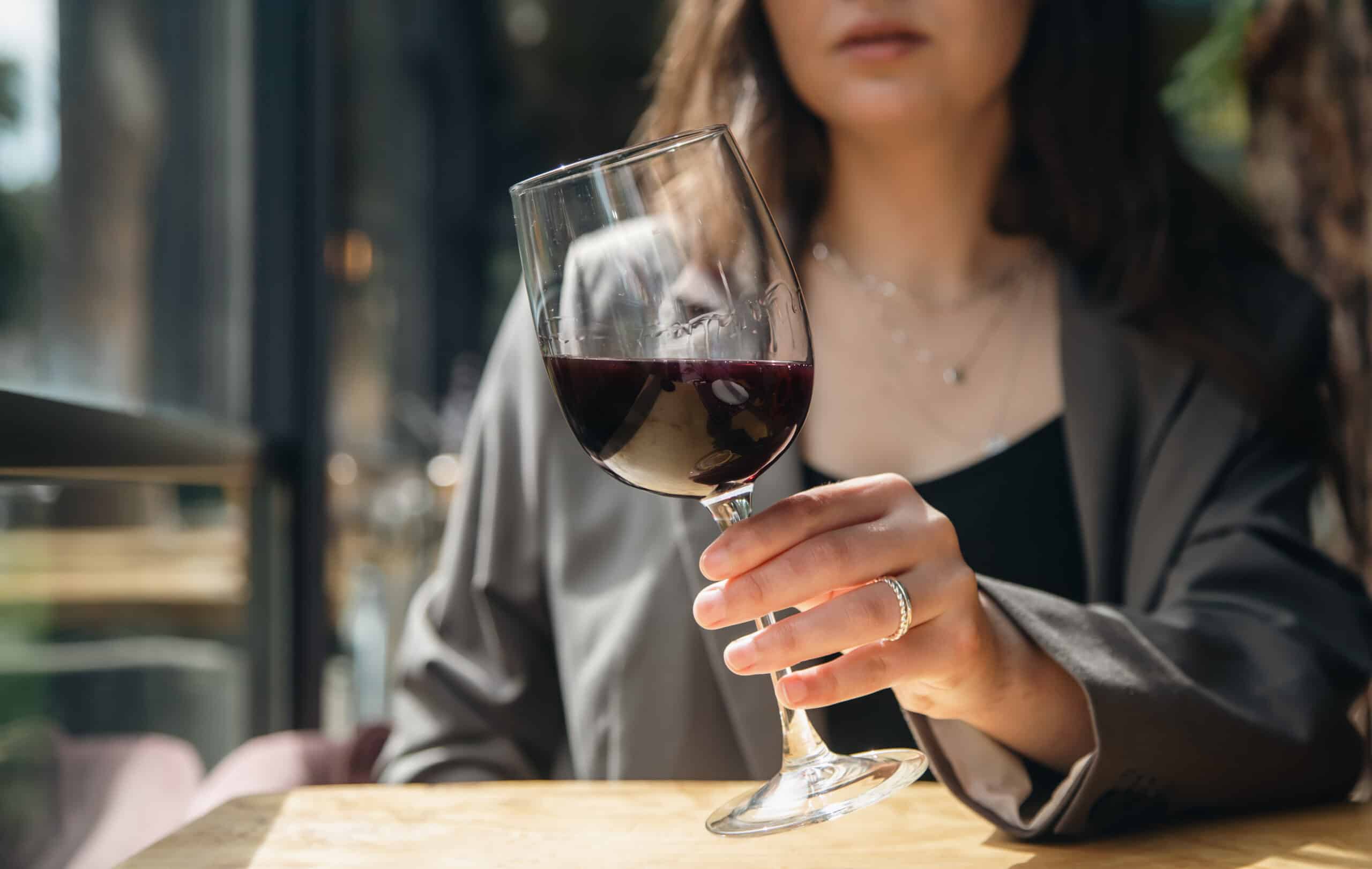 A woman holding a glass of wine in a restaurant wondering how long does wine stay in your system.