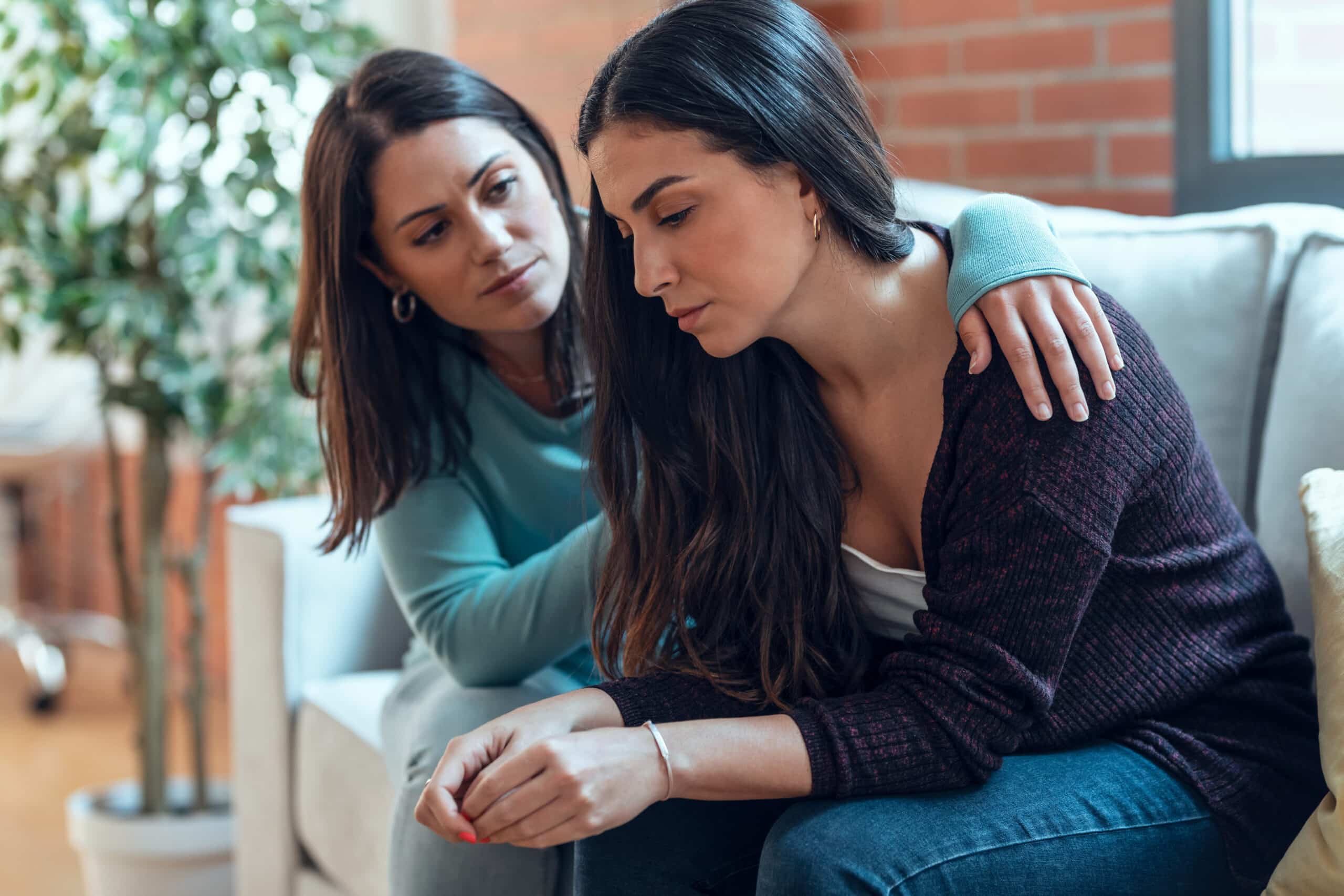 A woman comforts her friend on a couch for the topic can you force someone into rehab in california.